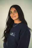 Model wearing close-up of the embroidered Alpine Inspired artwork on a crewneck sweatshirt.