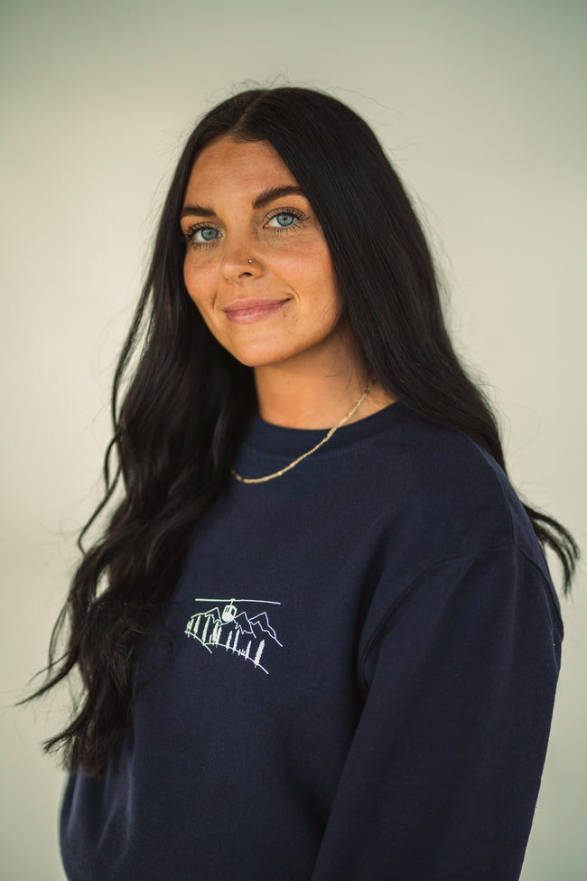 Model wearing close-up of the embroidered Alpine Inspired artwork on a crewneck sweatshirt.