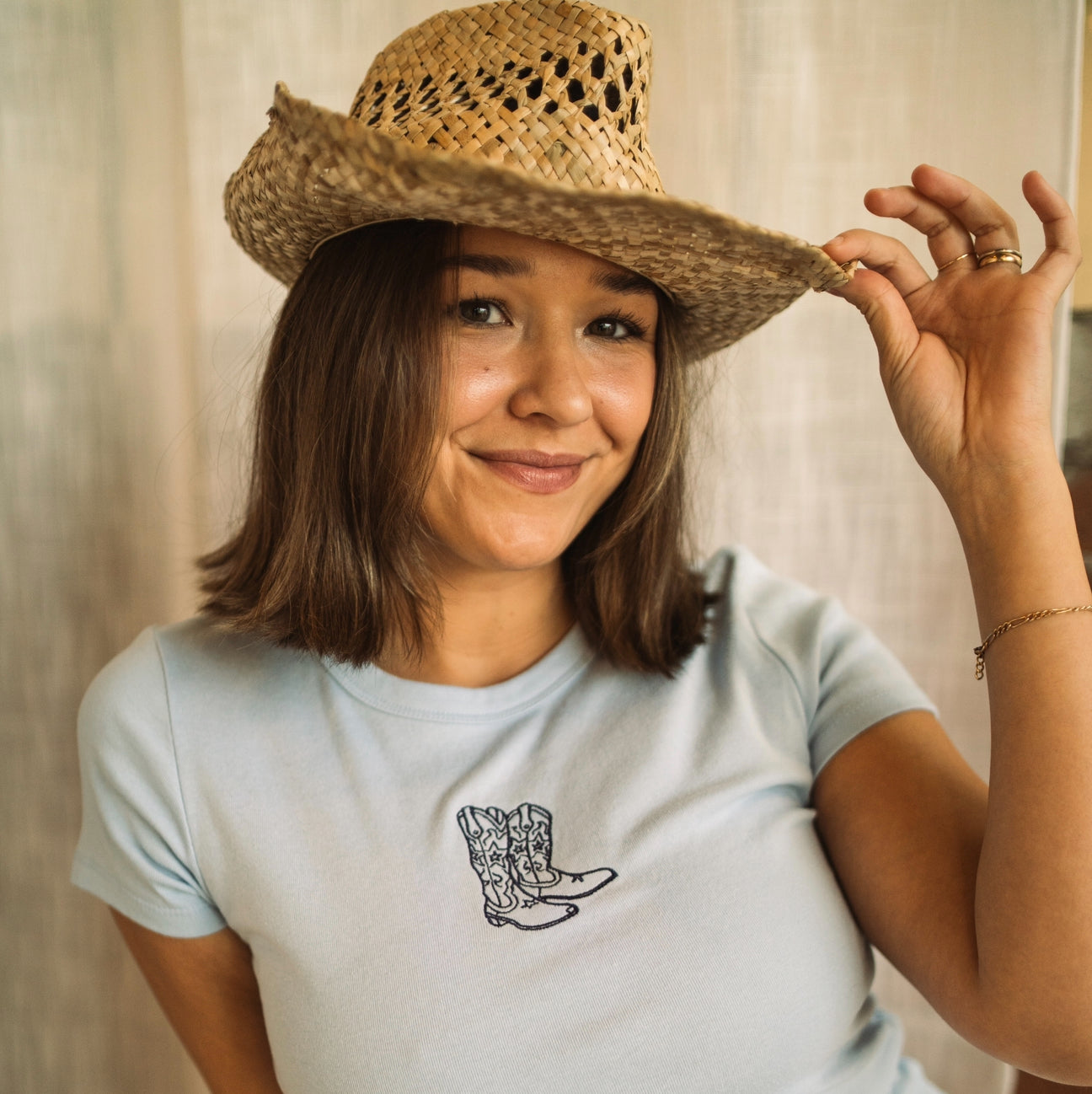 Model wearing a light blue embroidered cowgirl boots baby tee with a western-inspired cowboy hat.