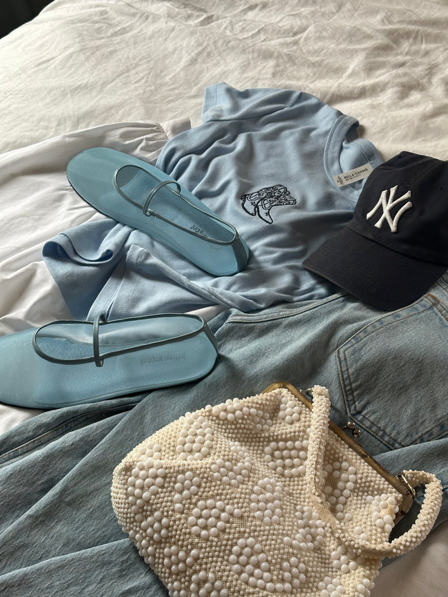 Stylized flat lay of light blue embroidered cowgirl boots baby tee with light wash denim, flats, and a navy cap.