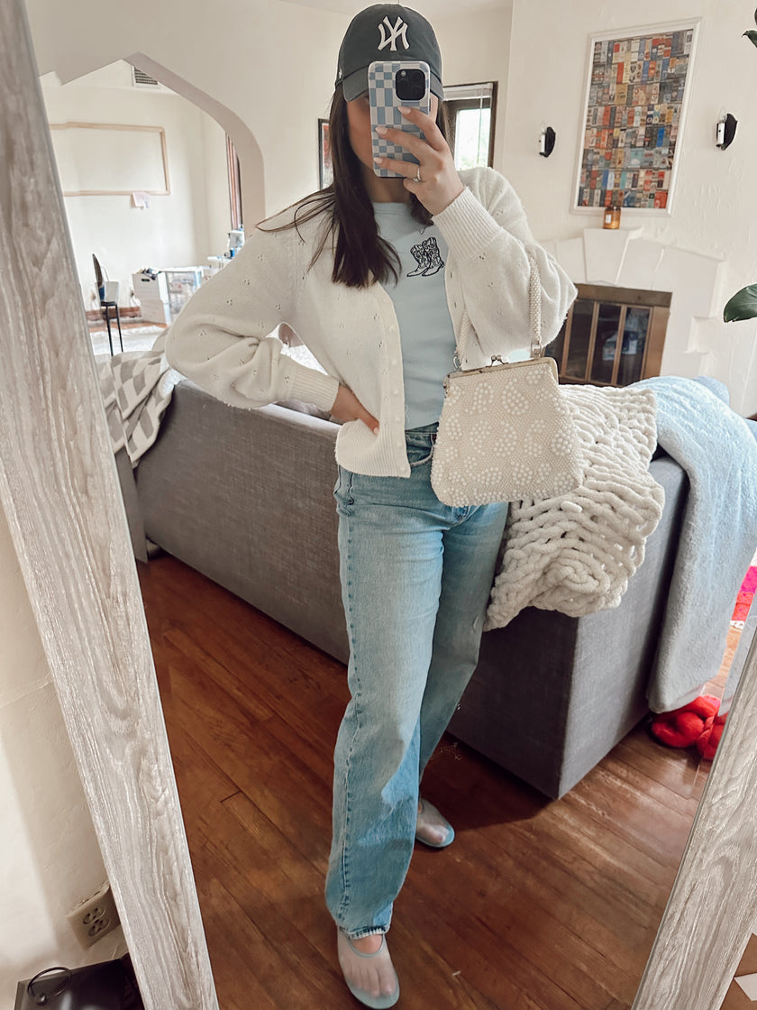 Model styling a light blue embroidered cowgirl boots baby tee with a cream knit cardigan and denim for a casual western-inspired outfit.