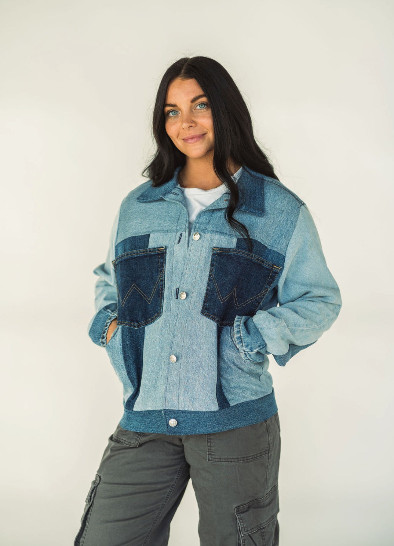 Model wearing a one-of-a-kind light wash patchwork denim jacket made from recycled jeans with contrasting dark denim pockets and snap-button closure.