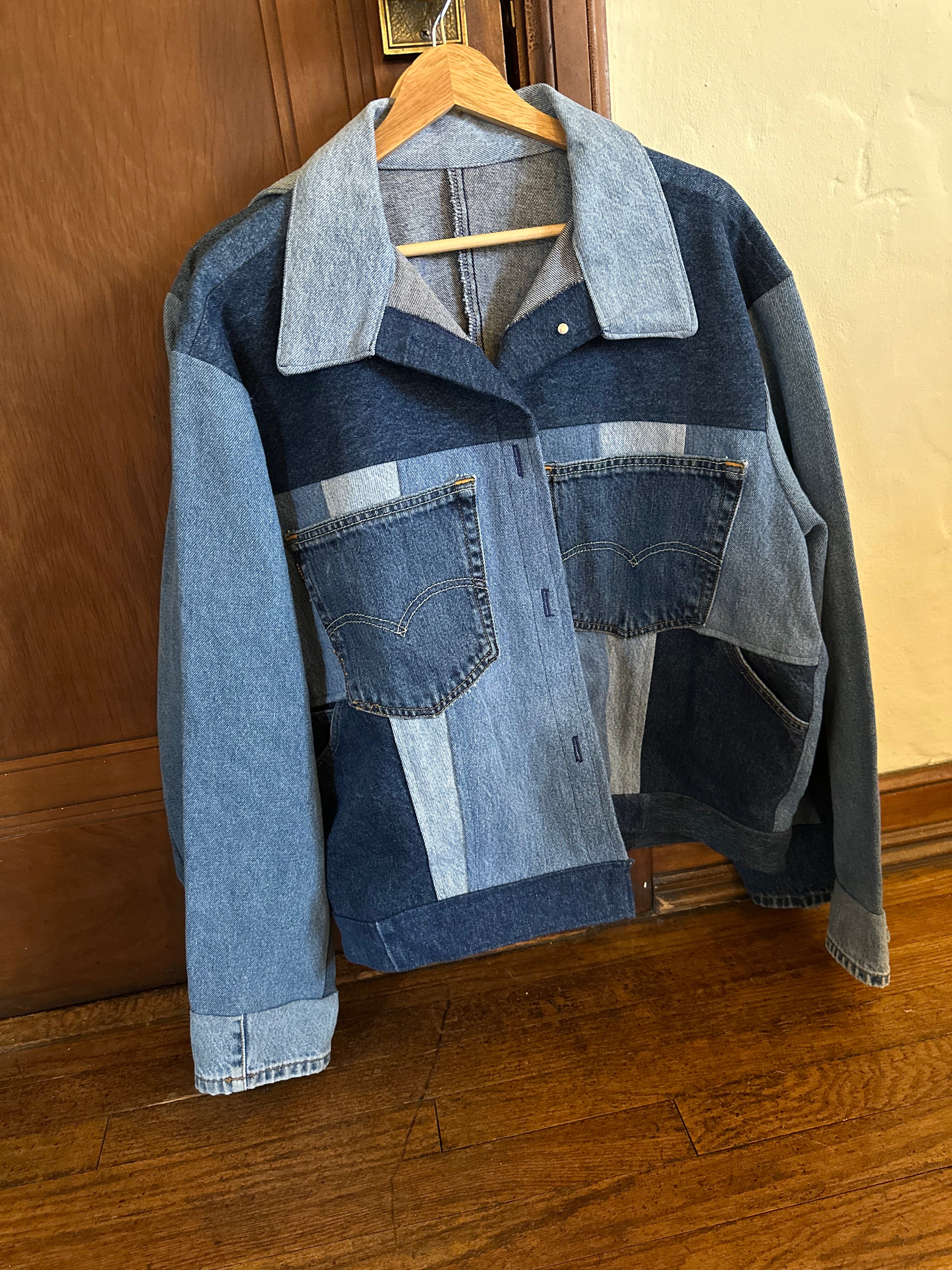 Front view of a one-of-a-kind patchwork denim jacket made from recycled jeans featuring contrasting light and dark wash denim, authentic vintage pockets, and a structured collar hanging on a wooden hanger.