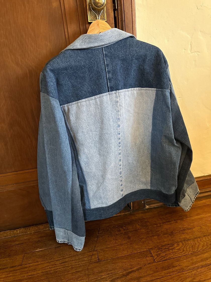 Back view of a one-of-a-kind patchwork denim jacket made from recycled jeans featuring contrasting light and dark wash denim panels, a minimalist color-block design, and a structured collar.