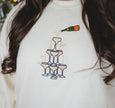 Close-up of the embroidered champagne tower graphic on a cream crewneck sweatshirt.