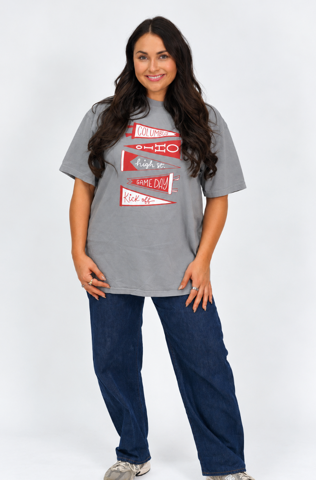 Woman wearing a gray graphic T-shirt featuring red and white pennant designs with “Columbus,” “Ohio,” “High St.,” “Game Day,” and “Kickoff” lettering.