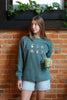Woman wearing a forrest green crewneck sweatshirt with embroidered coffee icons.