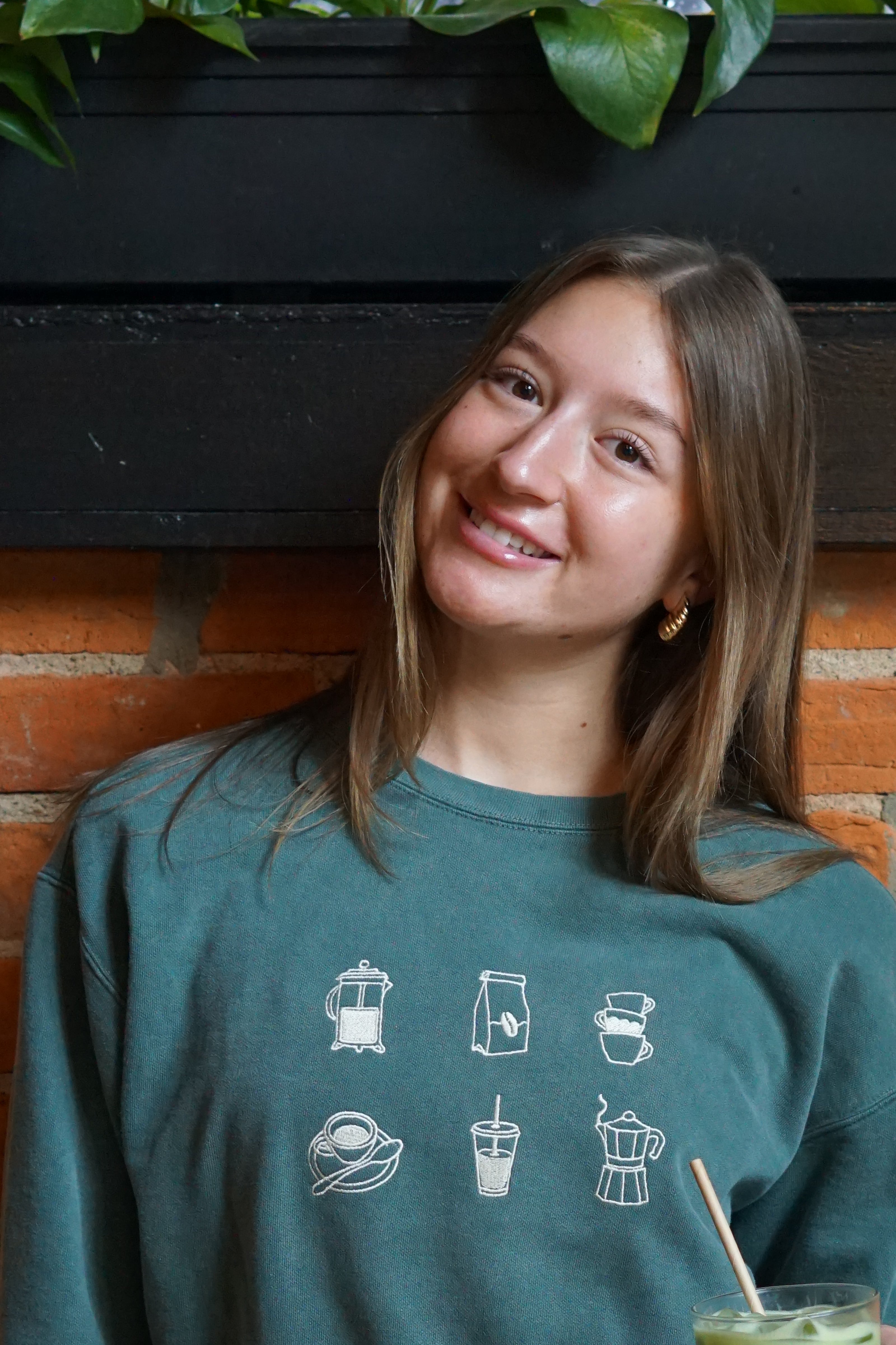 Close up of model wearing a forrest green crewneck sweatshirt with embroidered coffee icons.