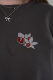 Close-up of the front chest of a charcoal gray sweatshirt, showing an embroidered 