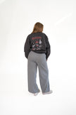 Woman standing against a white background from behind, wearing a charcoal gray crewneck sweatshirt with back game-day graphics, paired with wide-leg grey lounge pants.