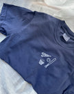 Flat lay of a navy Comfort Colors Columbus baseball T-shirt with embroidered CBUS pennant, baseball bat, baseball, and popcorn design.