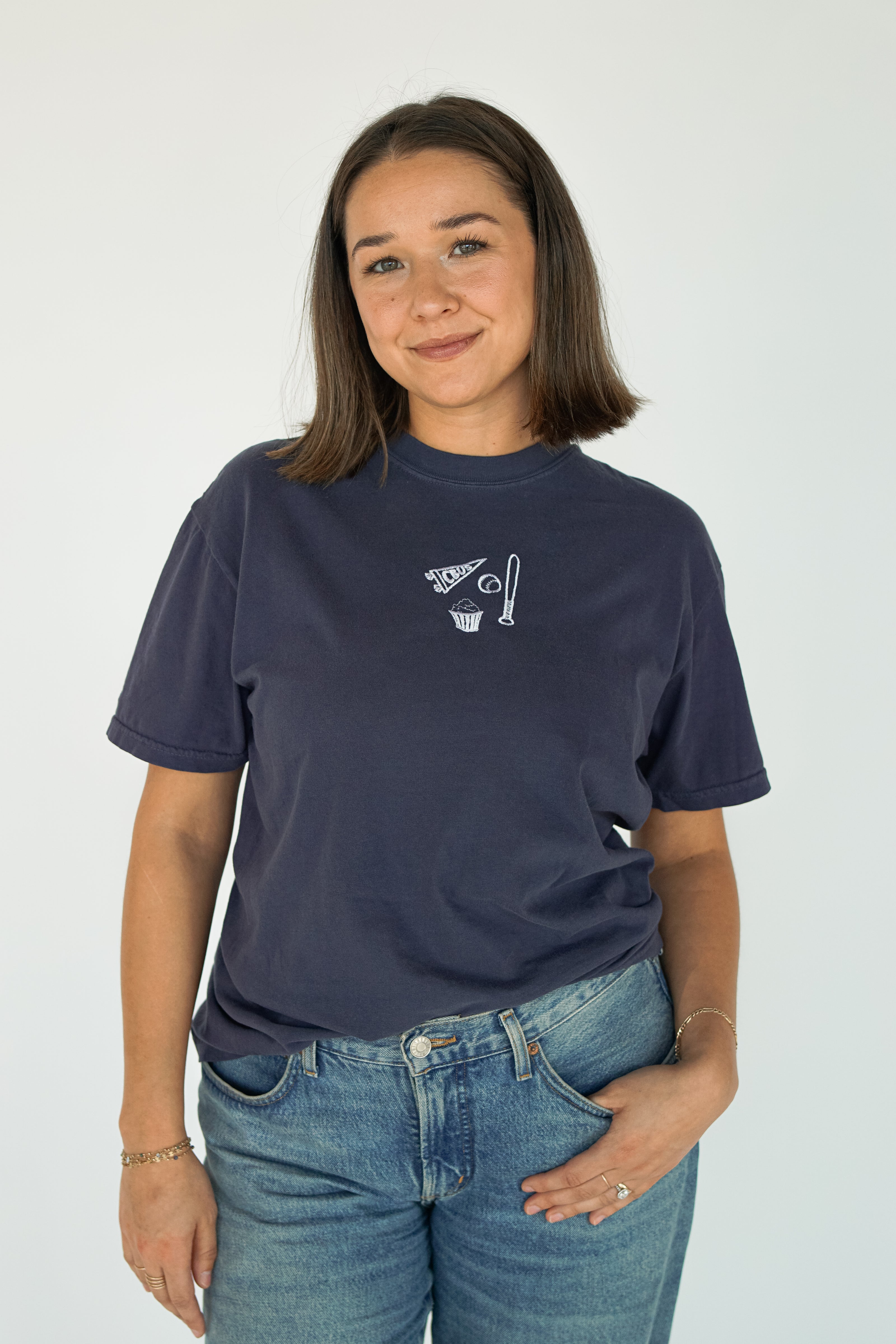 Woman wearing a navy embroidered Columbus baseball T-shirt featuring a CBUS pennant, baseball bat, baseball, and popcorn design.