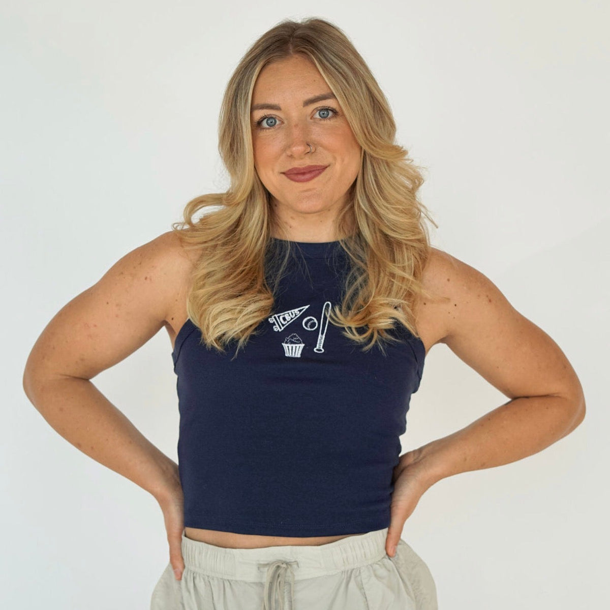 Woman wearing a navy embroidered Columbus hockey tank top featuring a CBUS pennant, hockey stick, puck, and popcorn design.