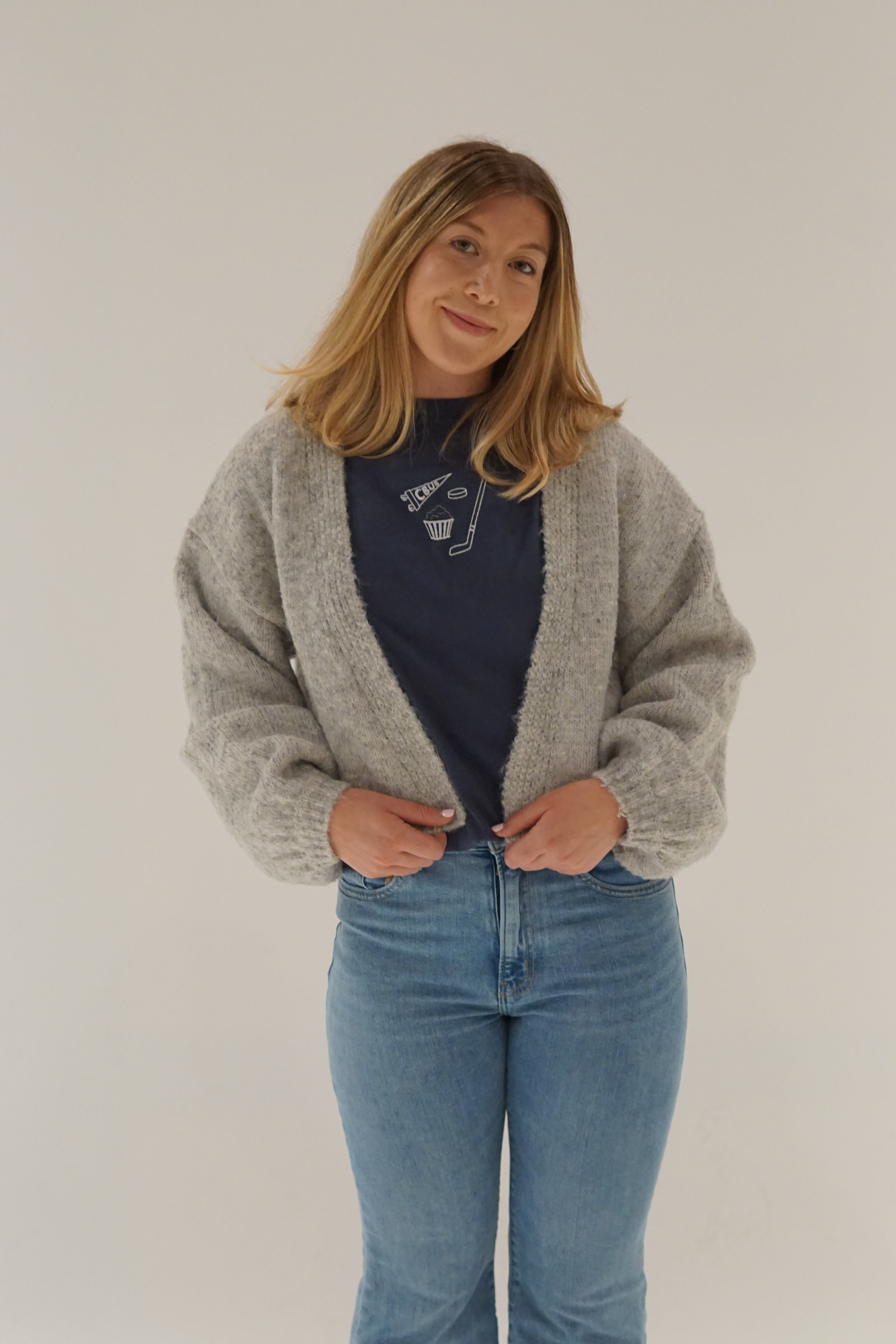 Model styling a navy embroidered Columbus hockey Comfort Colors T-shirt with a cozy gray cardigan and light wash denim for a casual game day outfit.