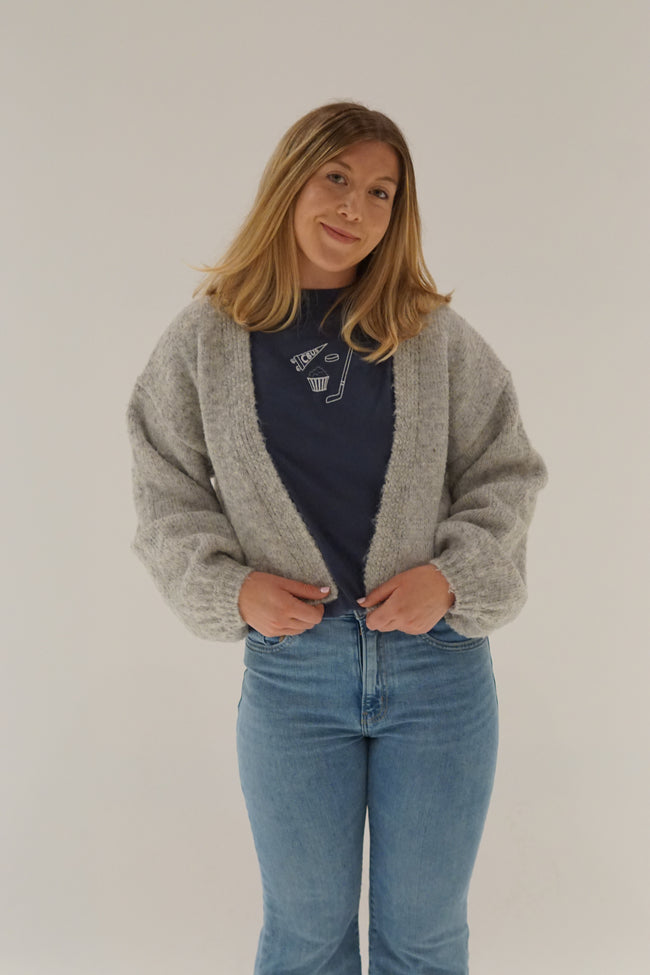 Model styling a navy embroidered Columbus hockey Comfort Colors T-shirt with a cozy gray cardigan and light wash denim for a casual game day outfit.