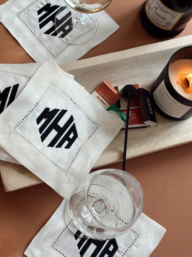 Personalized white linen cocktail napkins featuring a custom embroidered monogram for home entertaining and gifting.