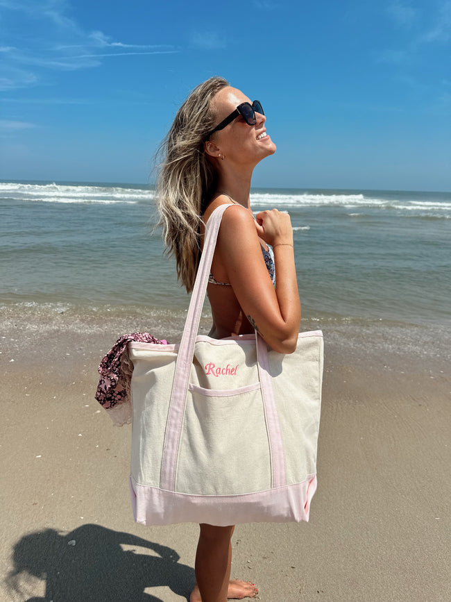 Woman carrying a personalized canvas beach tote embroidered with a name while walking along the beach.