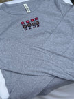 A folded heather gray long-sleeve shirt with a small chest graphic featuring four cartoon buckeyes holding red signs that spell 'OHIO'.