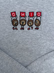 Close-up of a heather gray fabric surface with an embroidered graphic of four cartoon Ohio state silhouettes holding red signs that spell OHIO.