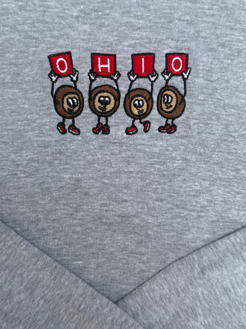 Close-up of a heather gray fabric surface with an embroidered graphic of four cartoon Ohio state silhouettes holding red signs that spell OHIO.