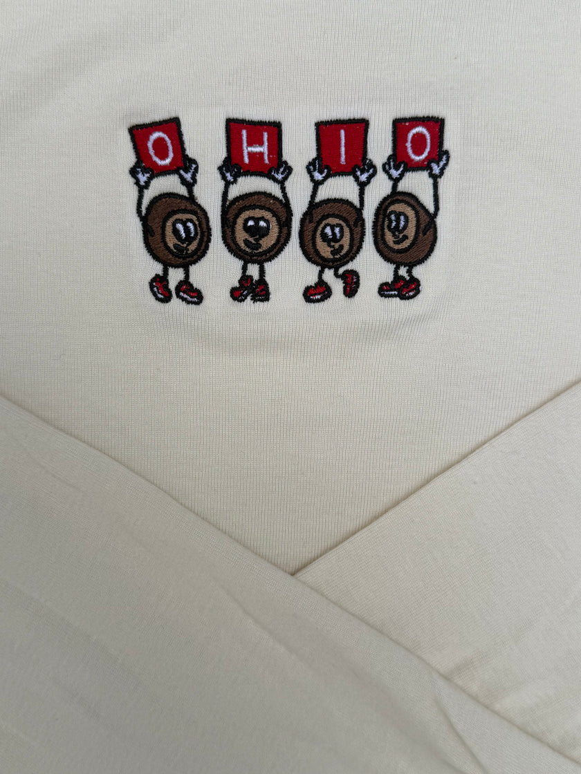 Close-up of a cream-colored fabric garment featuring an embroidered graphic of four cartoon characters holding red signs that spell 'OHIO'.