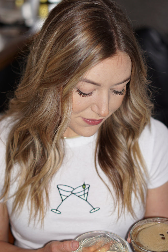 Model wearing the white Tini graphic t-shirt with green embroidery. 