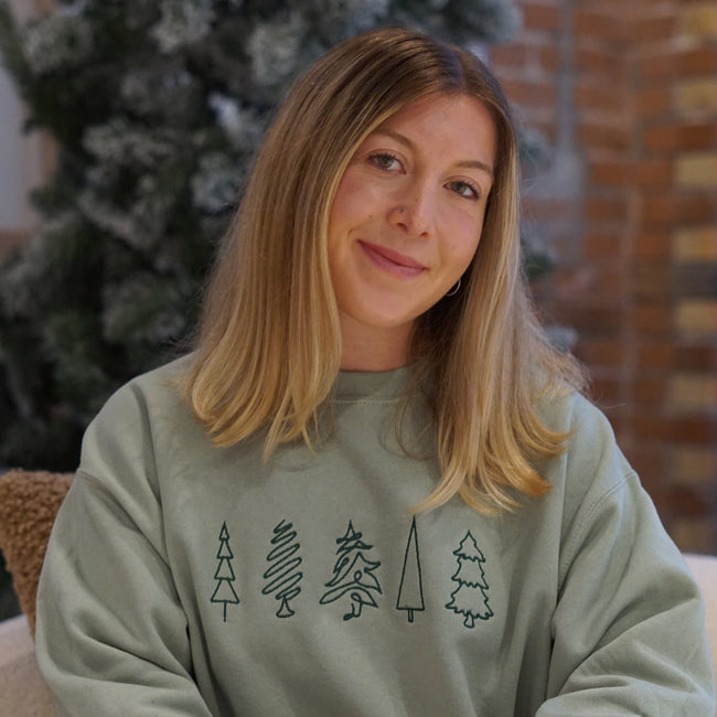 Woman wearing an embroidered Doodle Holiday Trees crewneck sweatshirt featuring whimsical Christmas tree designs.