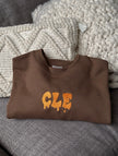 Folded brown crewneck sweatshirt featuring the embroidered Drip CLE design.