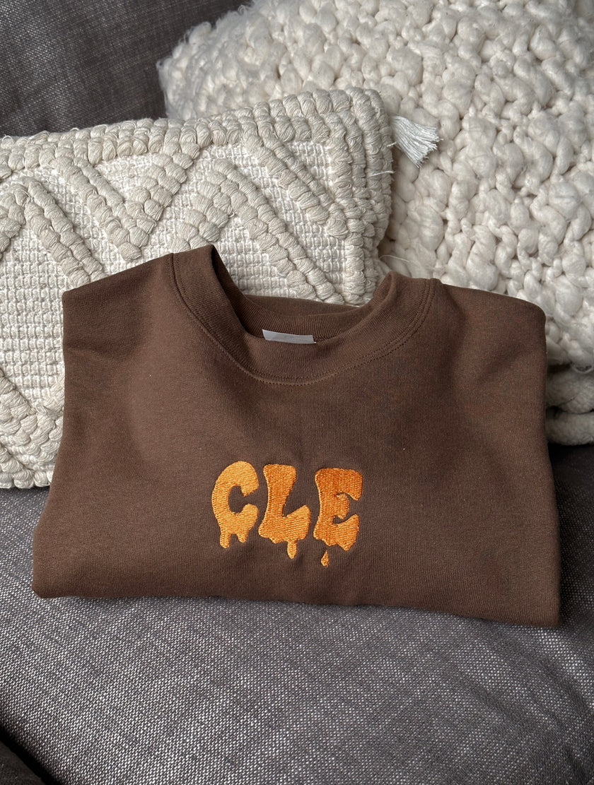 Folded brown crewneck sweatshirt featuring the embroidered Drip CLE design.