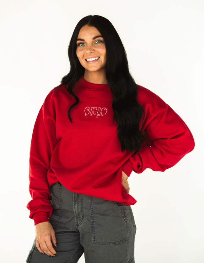 Model wearing a red crewneck sweatshirt embroidered with the Capsule Collective Drip Ohio design.