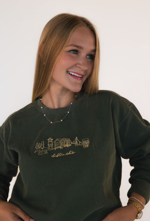 Woman wearing a dark green T-shirt with an embroidered Dublin, Ohio skyline and “dublin, ohio” lettering on the chest.