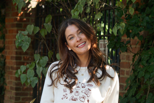 Woman wearing an ivory Fall Essentials graphic crewneck sweatshirt featuring autumn-inspired icons.