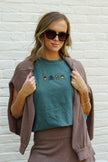Woman wearing a green Fall Essentials embroidered T-shirt featuring autumn-inspired icons, styled with a cardigan.