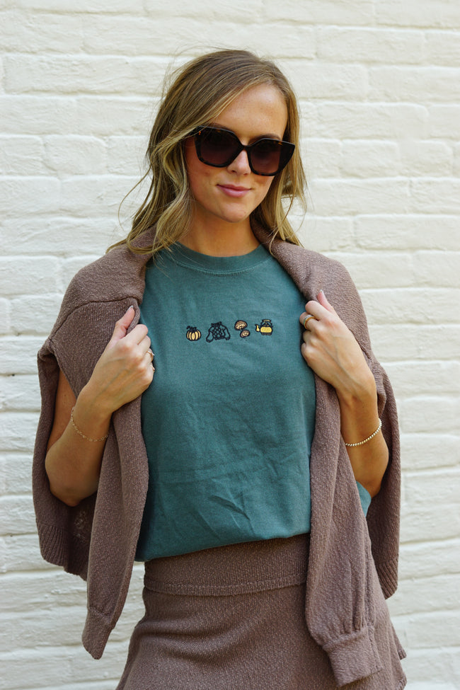 Woman wearing a green Fall Essentials embroidered T-shirt featuring autumn-inspired icons, styled with a cardigan.