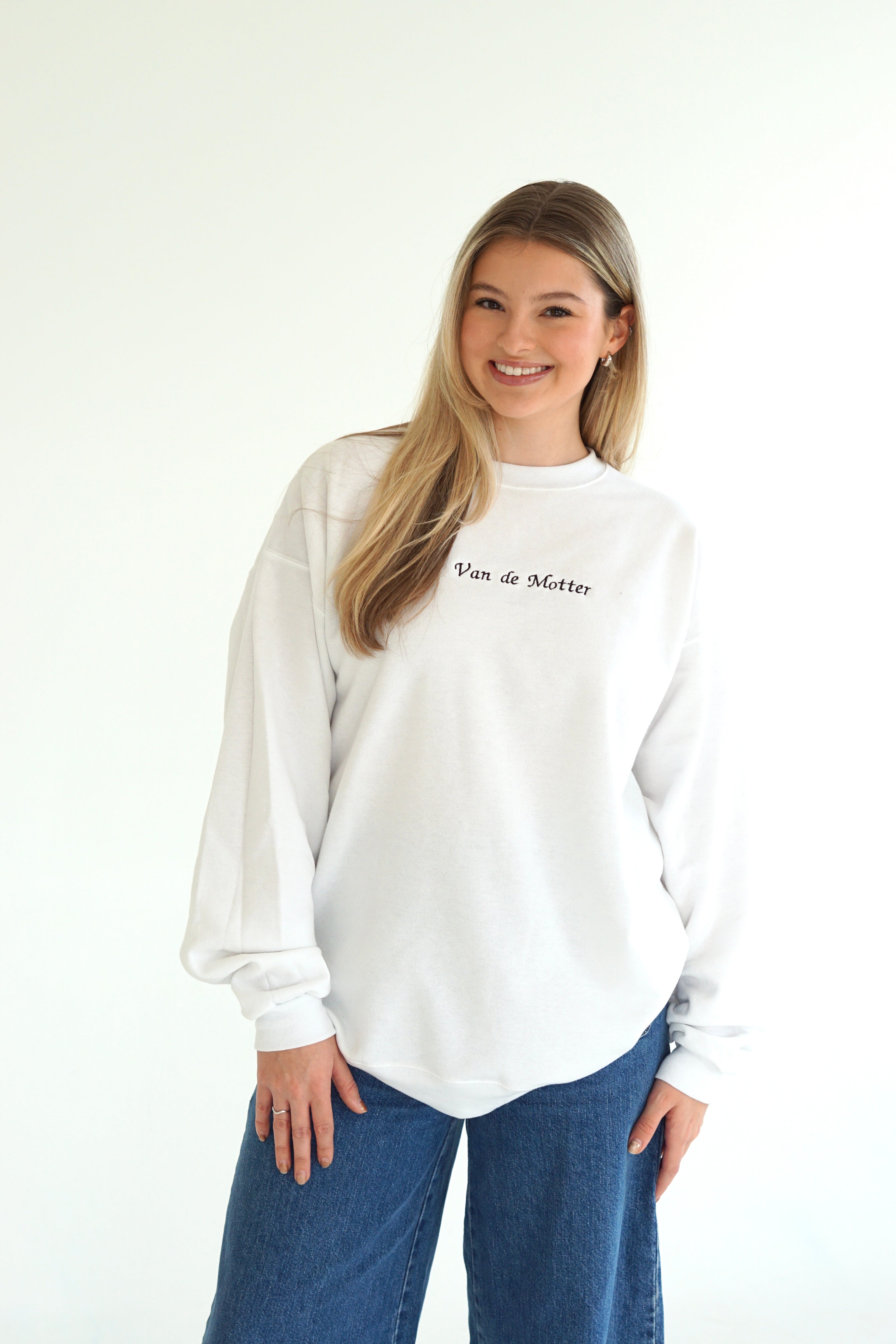 Woman wearing a white personalized crewneck sweatshirt embroidered with a custom future last name in black script.