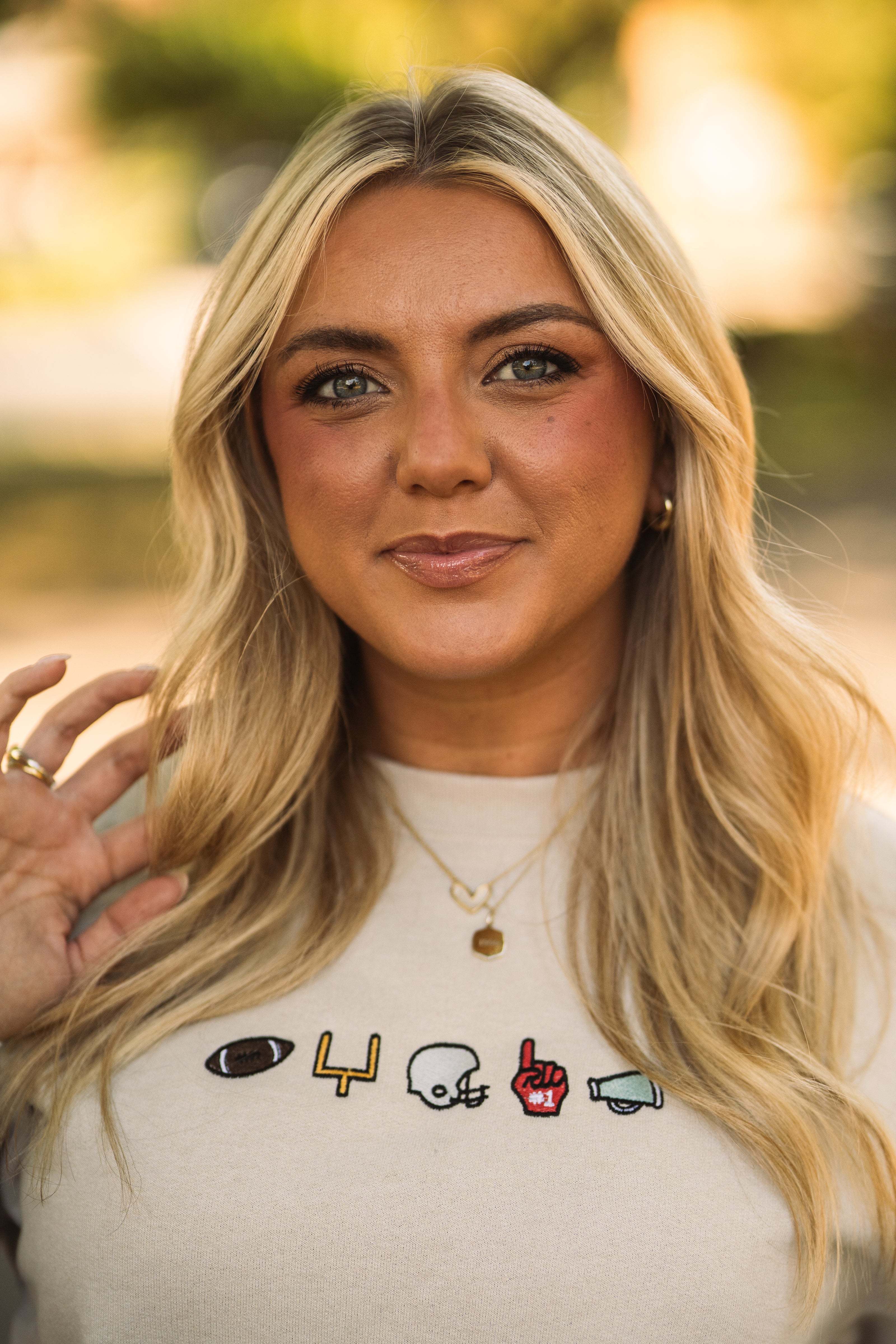 Model wearing a cream Ohio football crewneck featuring embroidered game day icons including a football, goal post, helmet, foam finger, and megaphone.