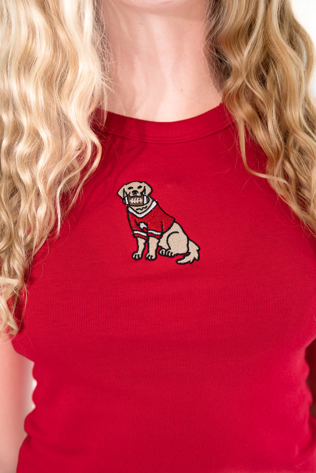  Blonde woman standing against a white background, wearing a bright red ribbed high-neck tank top with an embroidered dog patch.