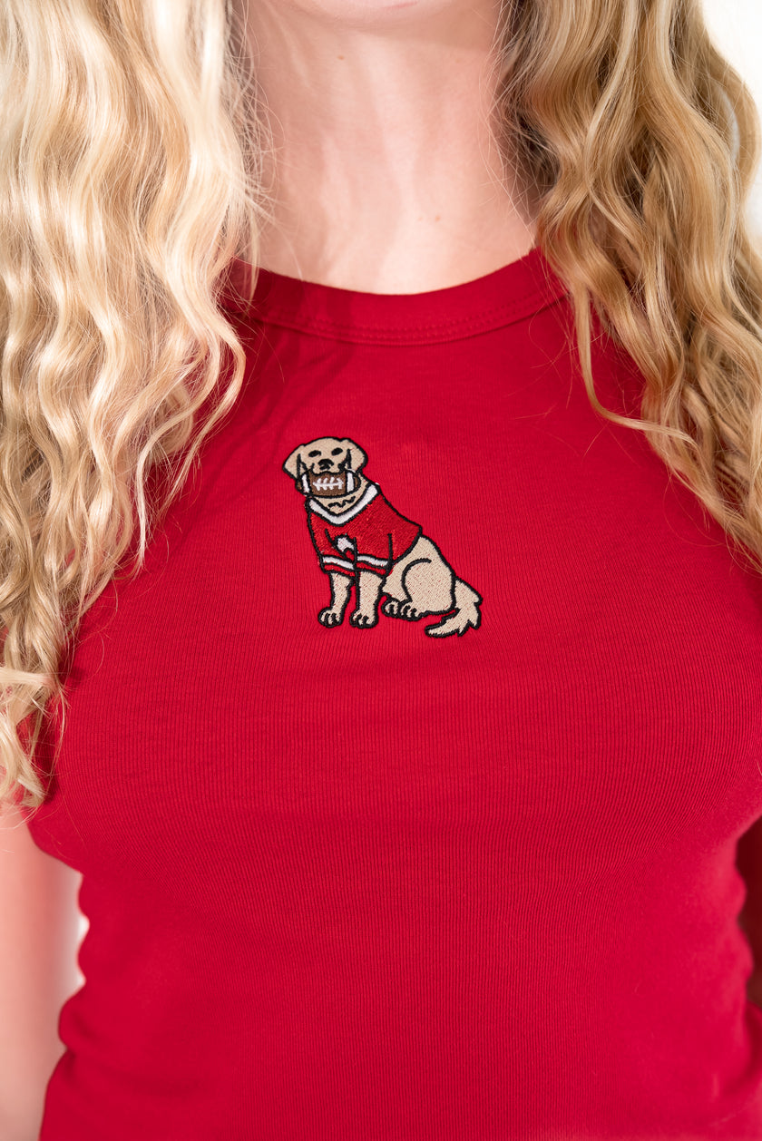  Blonde woman standing against a white background, wearing a bright red ribbed high-neck tank top with an embroidered dog patch.