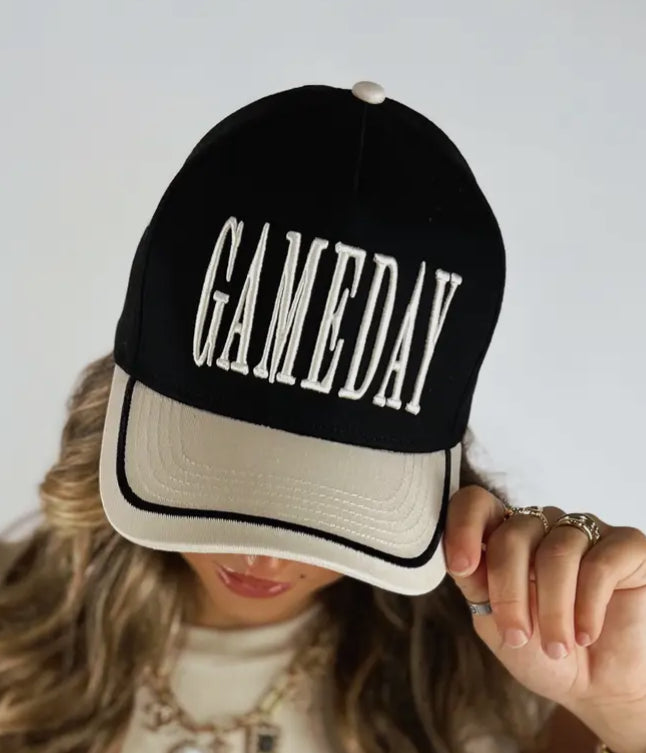 Black and beige cap with 'GAMEDAY' text held by a person against a light background