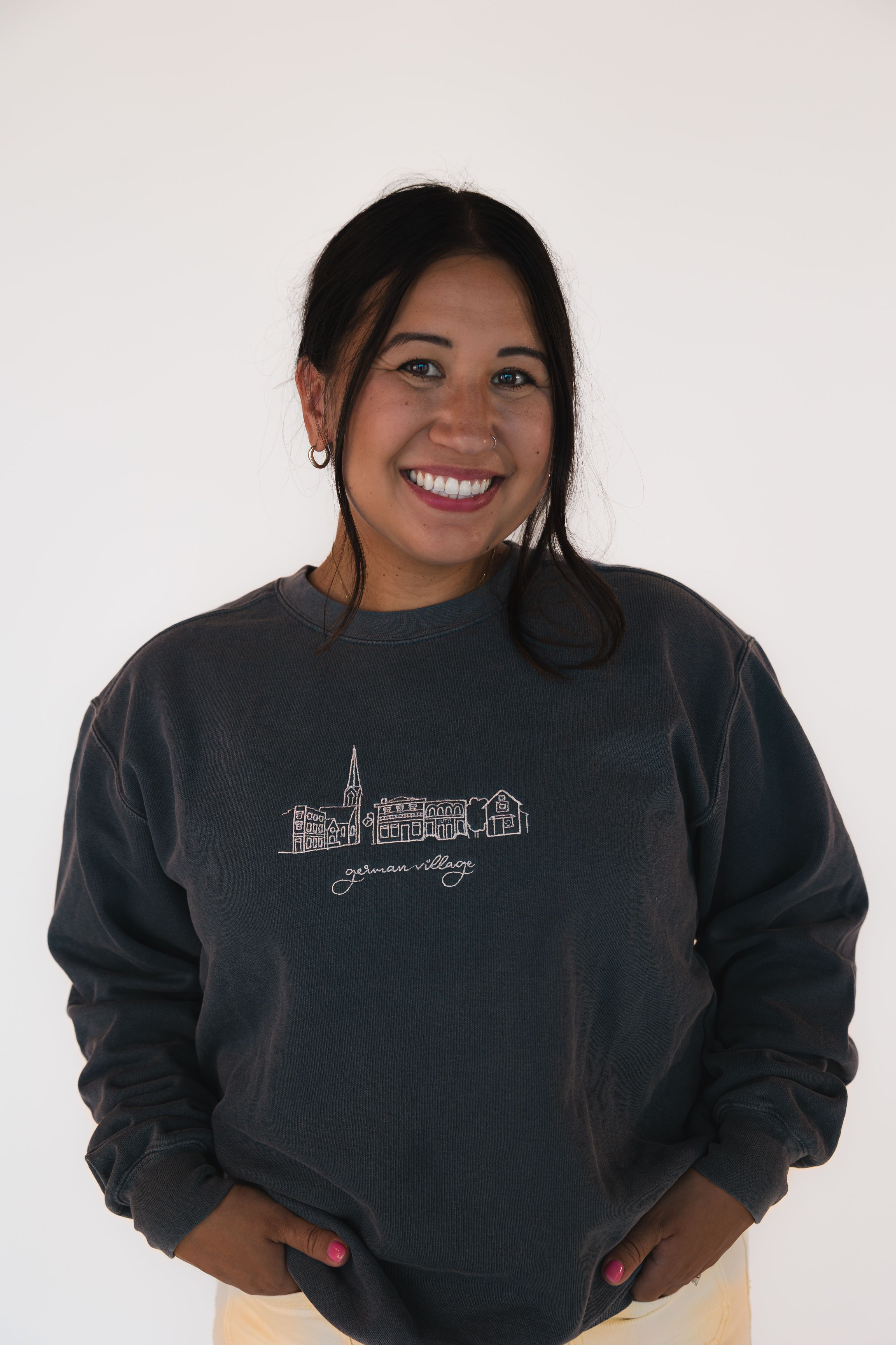 Woman wearing a charcoal German Village embroidered crewneck sweatshirt with a Columbus neighborhood skyline design.