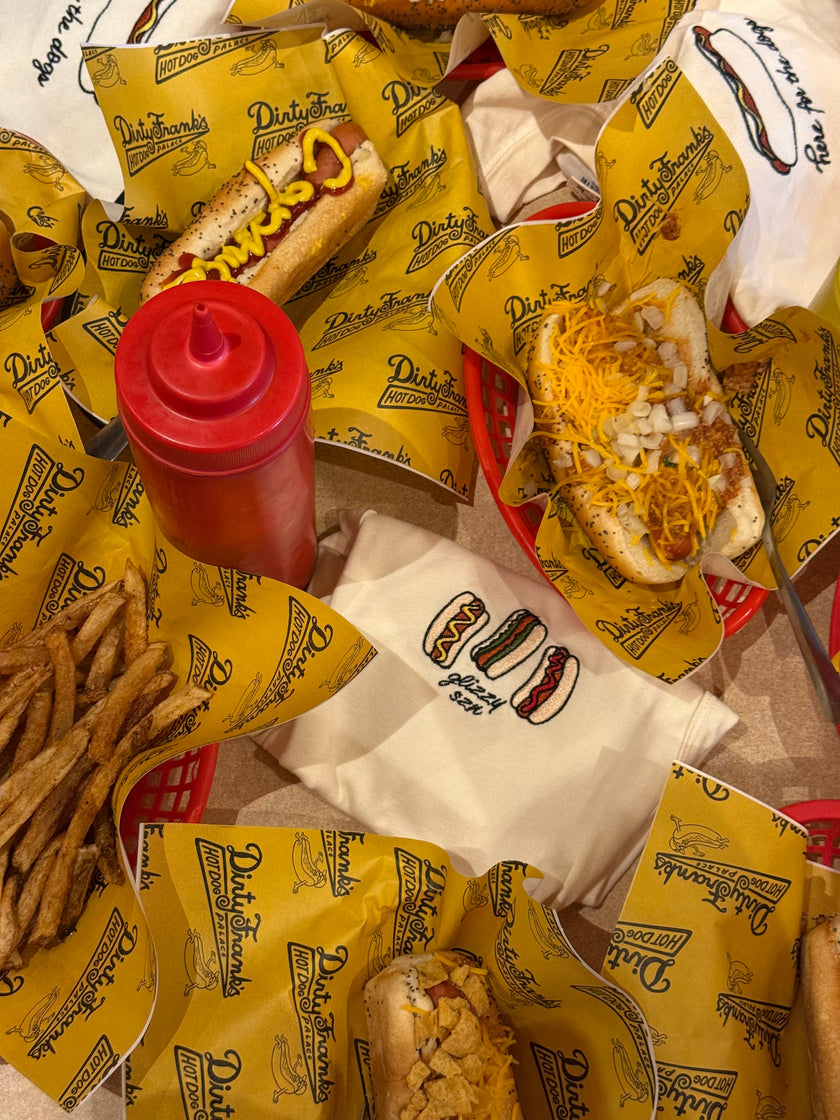 Flat lay of the Glizzy Season embroidered tank surrounded by hot dogs, fries, and classic diner food.