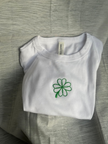 White fitted baby tee with green embroidered four-leaf clover design.