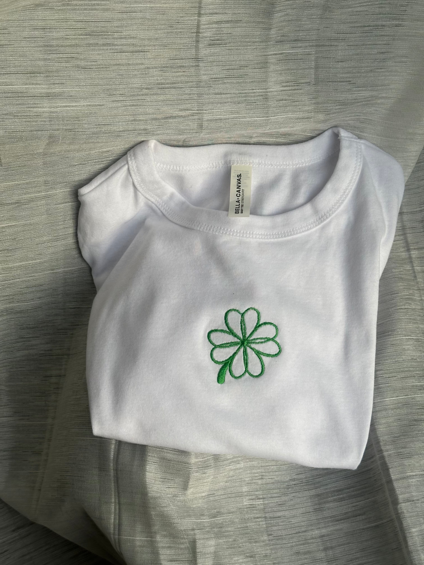 White fitted baby tee with green embroidered four-leaf clover design.