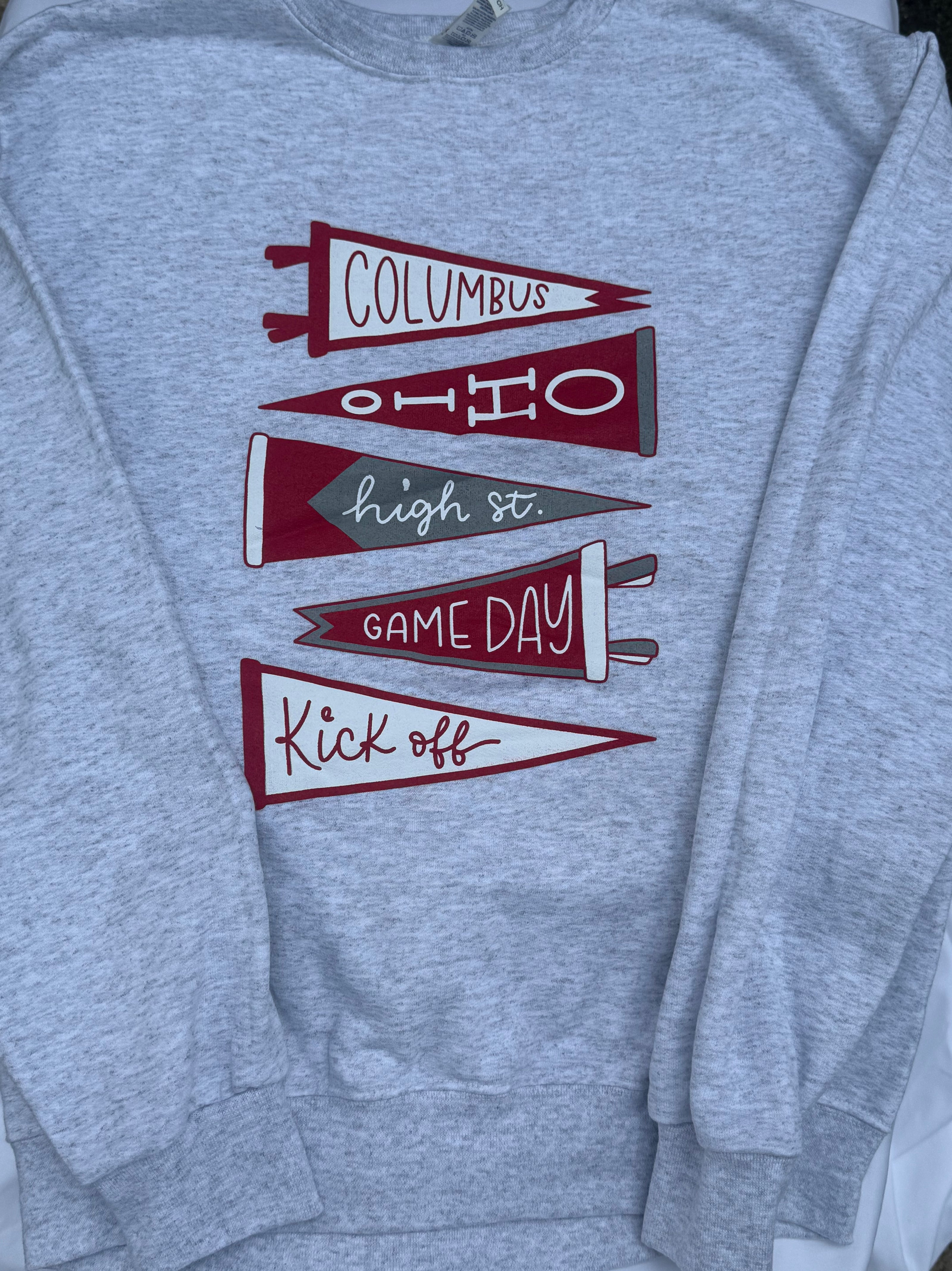 A heather gray crewneck sweatshirt featuring a graphic of five red and gray pennants with text reading 'Columbus', 'Ohio', 'high st.', 'GAME DAY', and 'Kick off'.