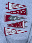 Close-up of a heather gray sweatshirt featuring a graphic print of five overlapping sports pennants in maroon and gray with white lettering that reads 'COLUMBUS', 'OHIO', 'high st.', 'GAME DAY', and 'Kick off'.
