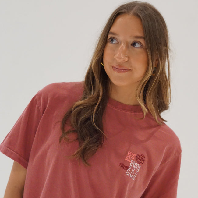 Woman wearing a holiday embroidered tee featuring a vintage-inspired Christmas postage stamp design.