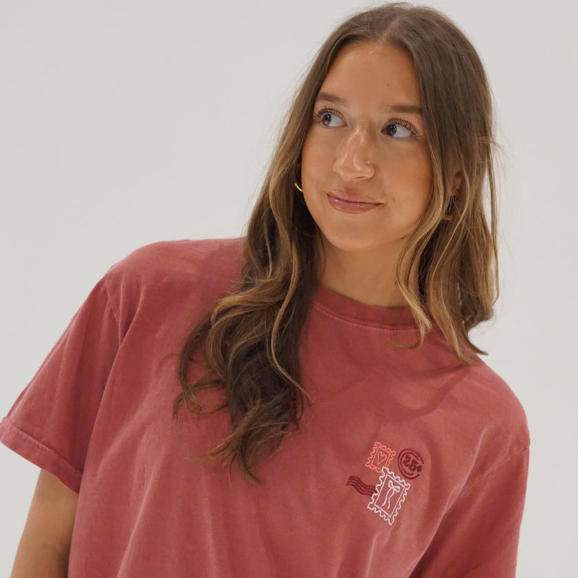 Woman wearing a holiday embroidered tee featuring a vintage-inspired Christmas postage stamp design.