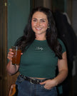 Woman wearing a forest green baby tee embroidered with white 