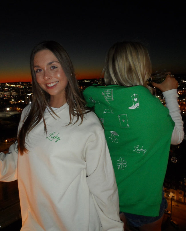 Woman wearing a cream crewneck with green embroidered “Lucky” lettering, styled for a St. Patrick’s Day celebration.