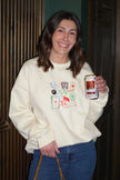 Woman wearing an ivory crewneck sweatshirt embroidered with colorful lucky-inspired icons.